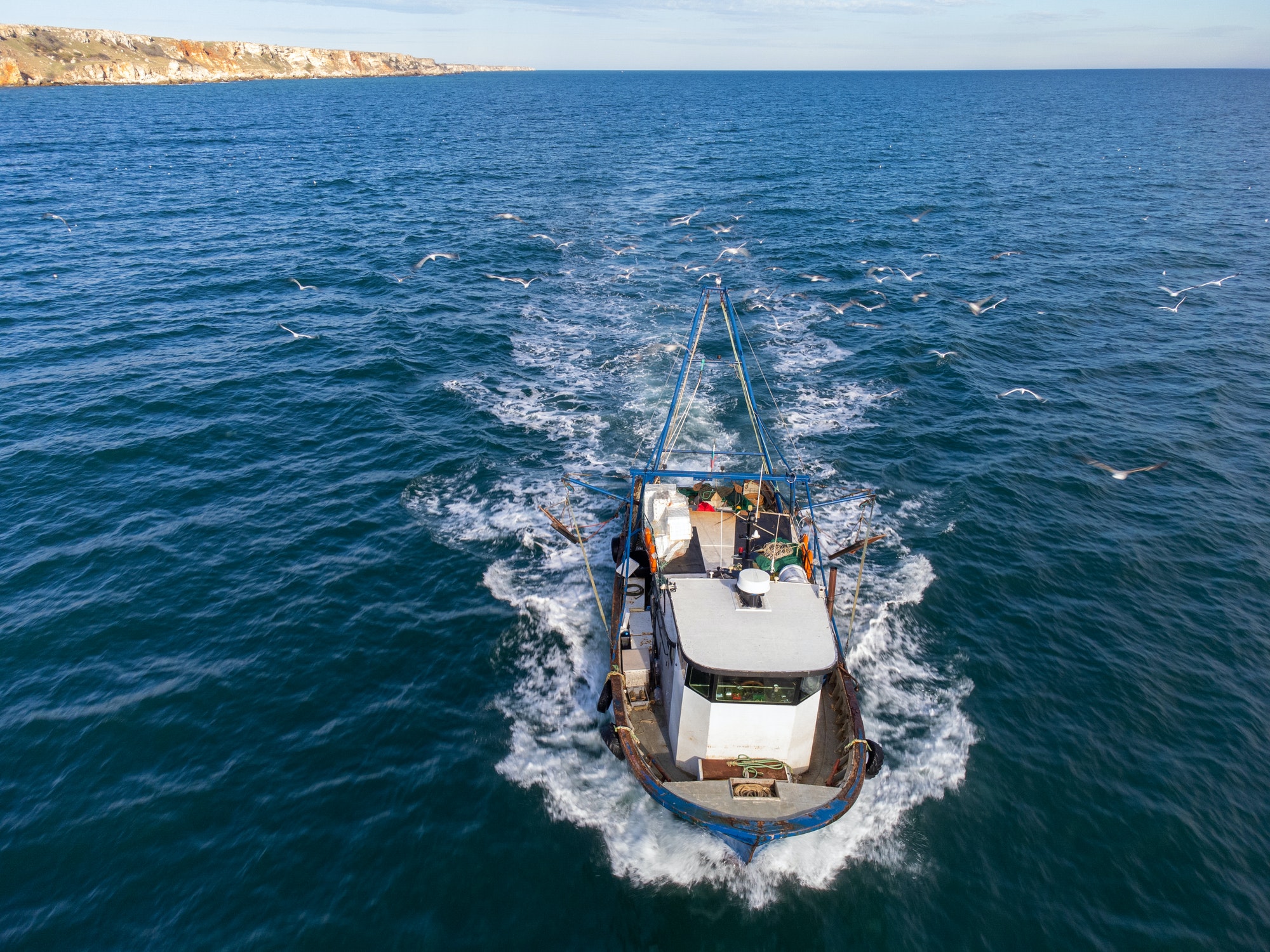 Fishing vessel boat floating in the blue sea, aerial view from drone.